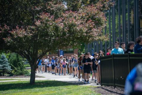 A photo of students lining up for New Orientation Day. They gather outside of the Dining Commons in rough rows of two.