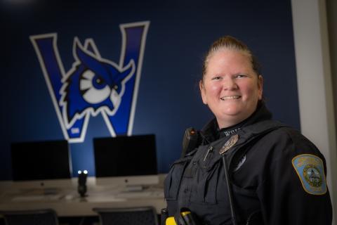 Officer McCue of Westfield State. She is wearing her police uniform and posing in front of a navy-blue Nestor mural.