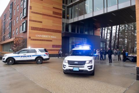 Two police vehicles are parked in front of University Hall, with a small crowd of people loading supplies for the Stuff-a-Cruiser event.