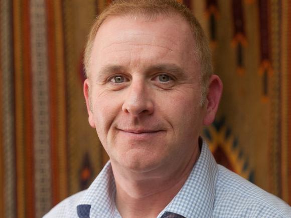 A white male standing in front of patterned wall decor