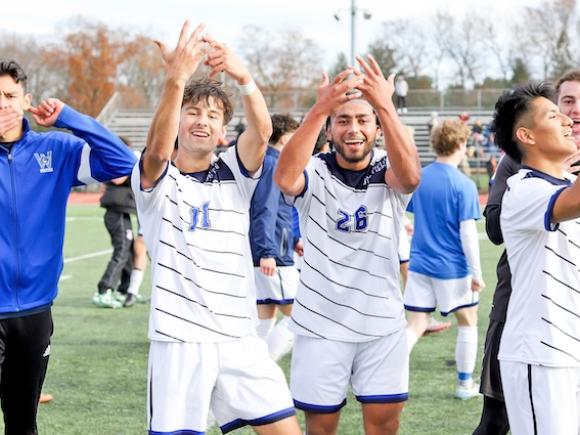 The Owls men's soccer team celebrating a game win by pointing to their ring finger, signaling their successful season.