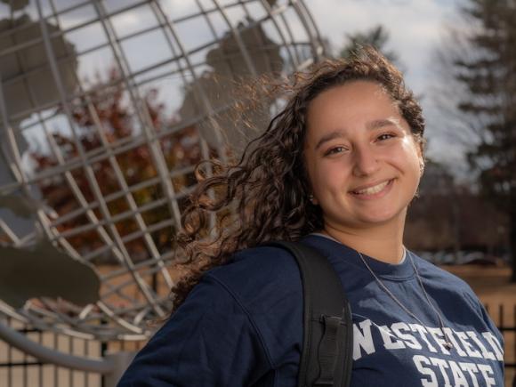 Stephanie Block, Class of 2025, a psychology major. She's posing in front of the campus globe and wearing a blue "Westfield State" shirt.