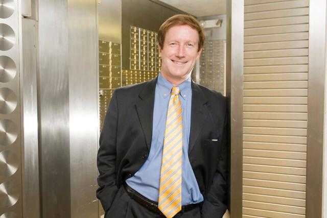 A person in a suit leans in the doorway at the entrance to a vault.