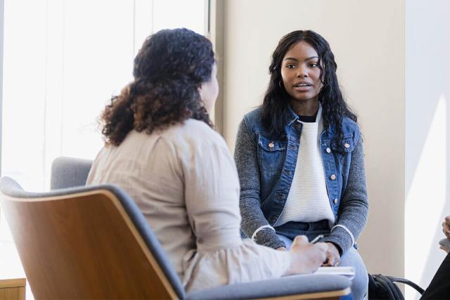 Two people conversing in a therapeutic setting while one takes notes.