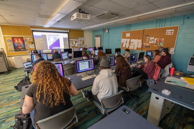 Students in a graphic design class with instructor giving a presentation.