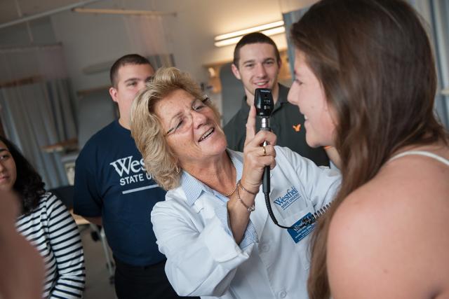 Multiple students in the Health Sciences program observe their professor demonstrating how to conduct an exam on a patient.