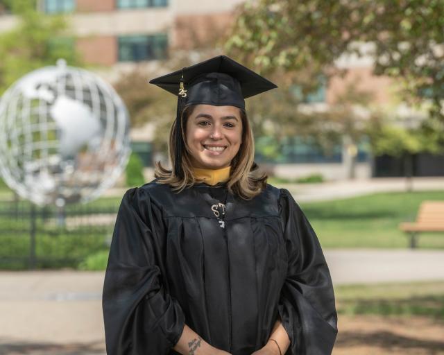 Student smiling in front of the campus globe wearing cap and gown.