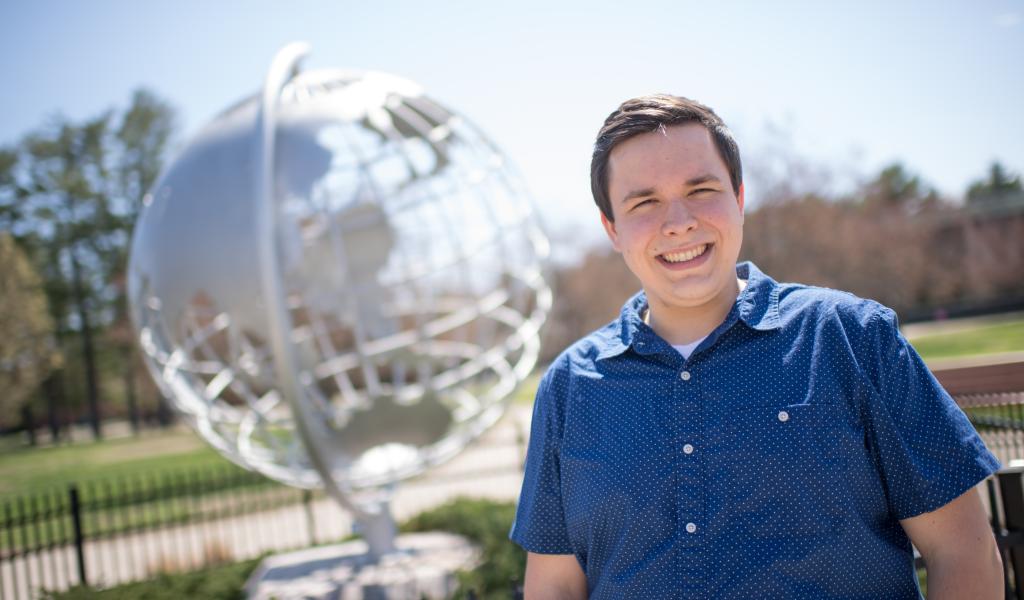 Photo of Aaron Lessing in front of the Globe sculpture one the campus green