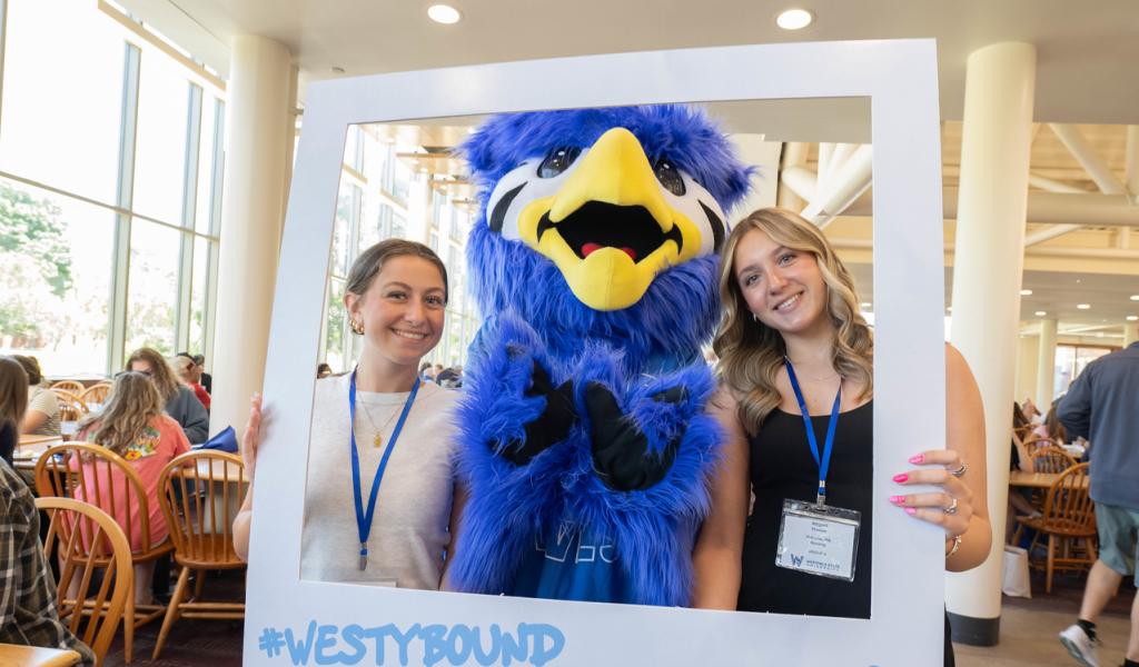 Two students at new student orientation smiling with campus mascot.