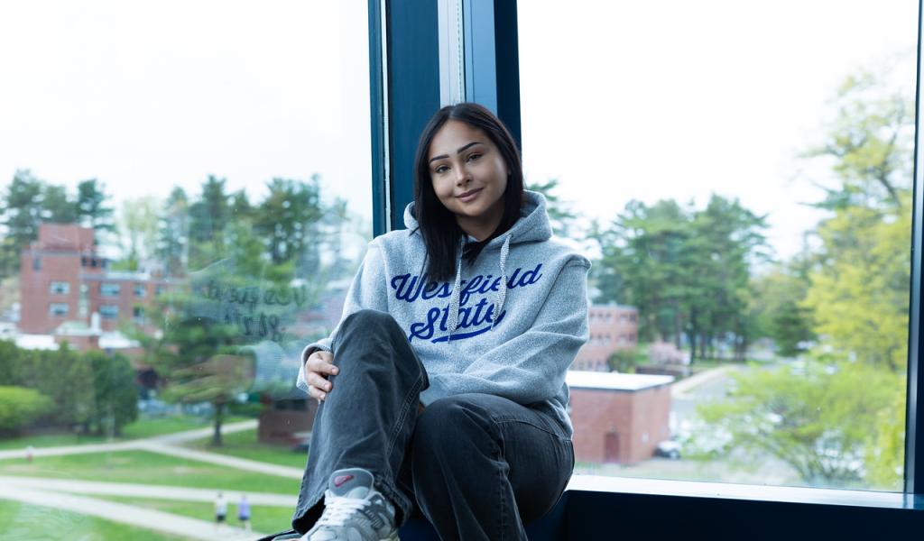 Student sitting in a campus building with a view of the campus green.