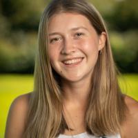 Student tour guide Shea Hamel. She is smiling and standing in an open field, with the background blurred behind her. 